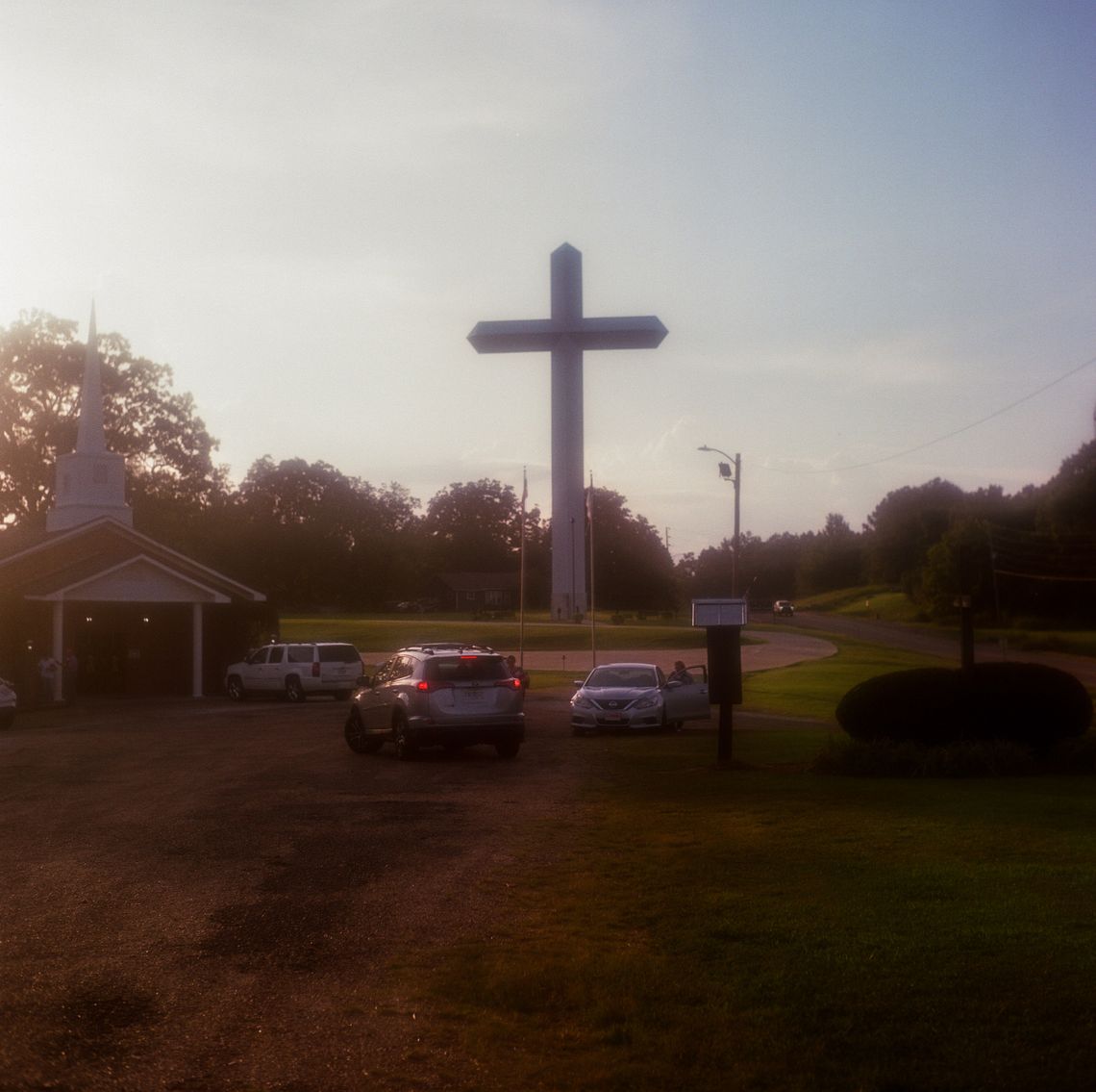 A triptych of three color photos of a large cross next to a road and a church. 
