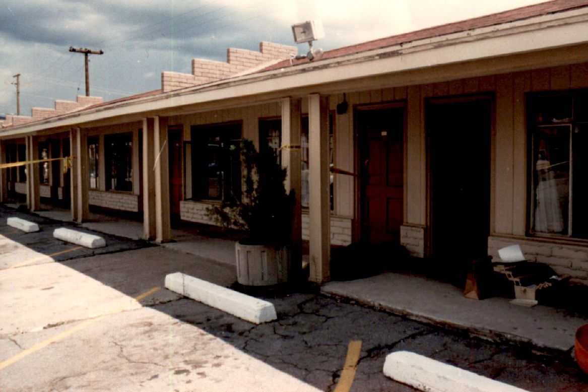 A one-story motel is situated behind a parking lot during the day. 