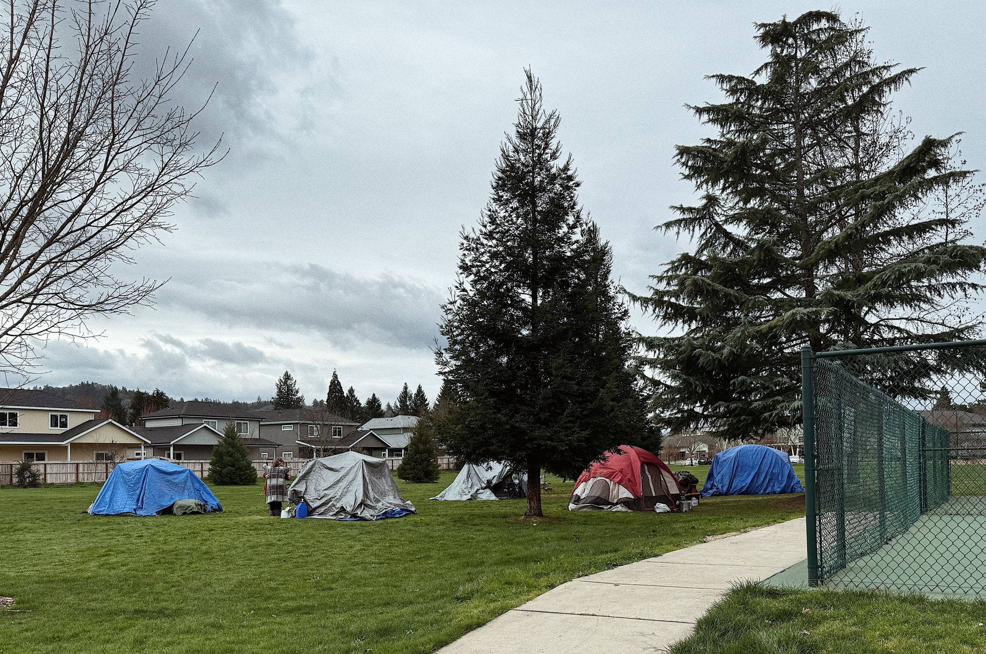 Multi-color tents are set up in a park in Grants Pass, Oregon.  Two people hug next to a tent.  