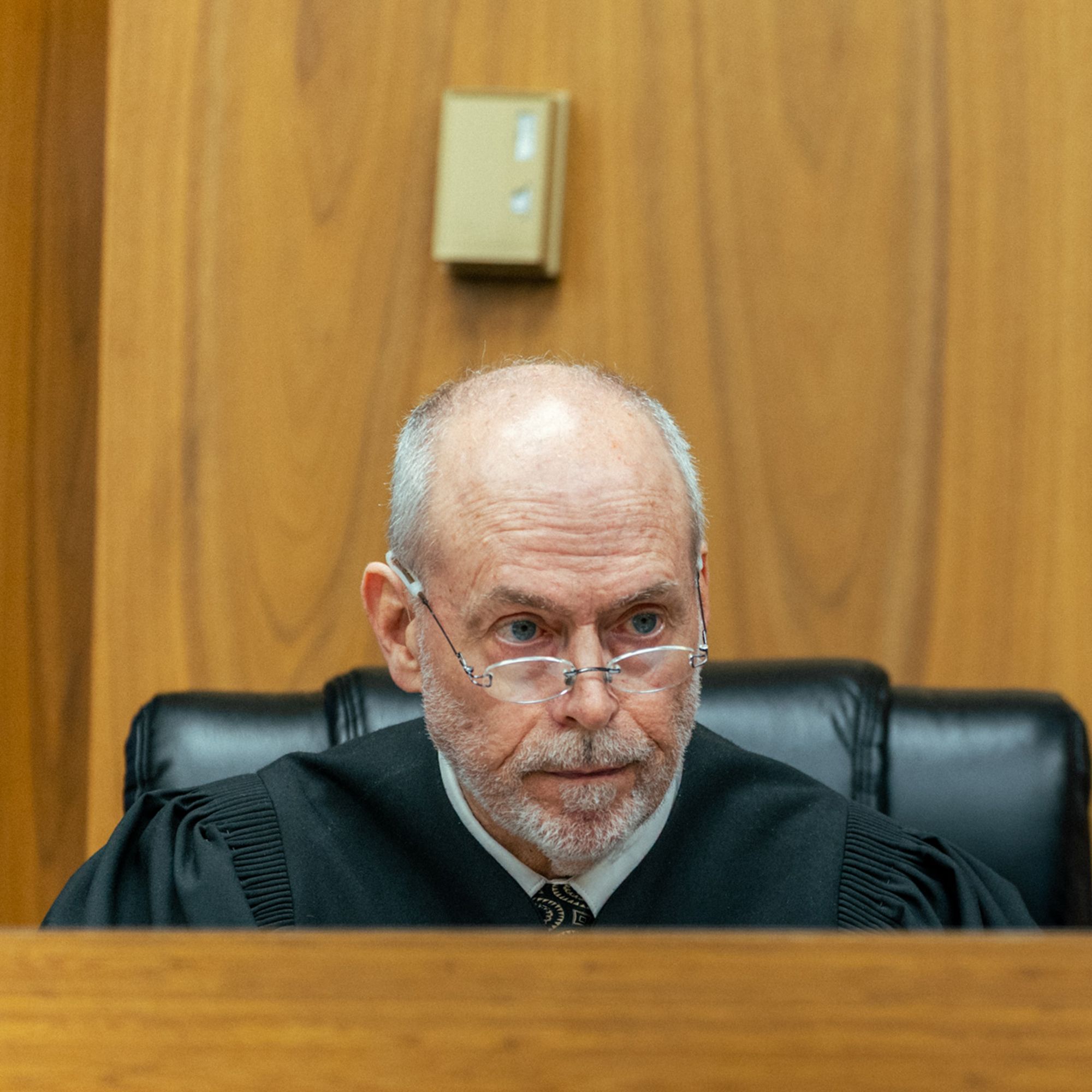 Right: A photo shows Judge Thomas Elwell, an elderly White man with glasses and a beard, in a courtroom. He is wearing a judge’s robe.