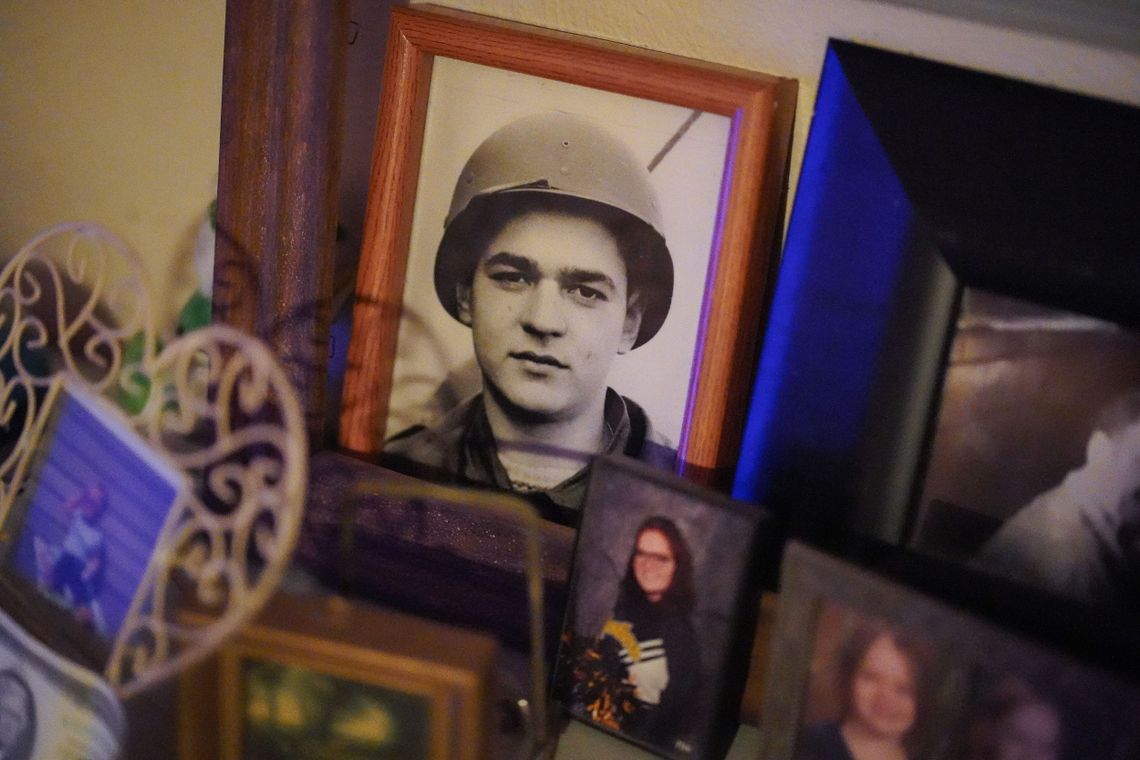 A black and white photograph of a young man in a military uniform and helmet is in a frame, among other framed pictures, including of Kathy Stoz-Silvis, from when she was 17. 