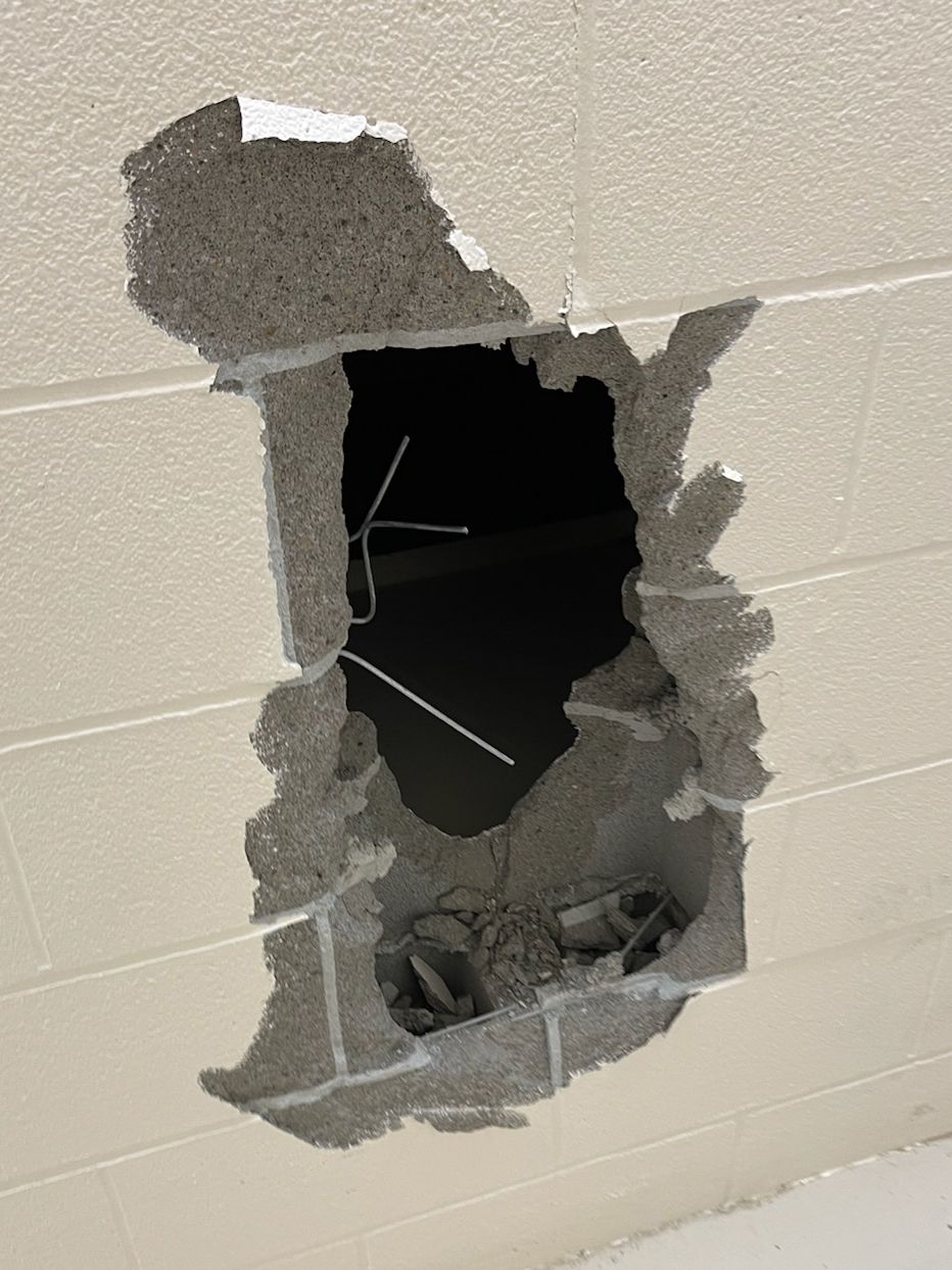 A photo shows a hole in a concrete wall, with exposed wires. 