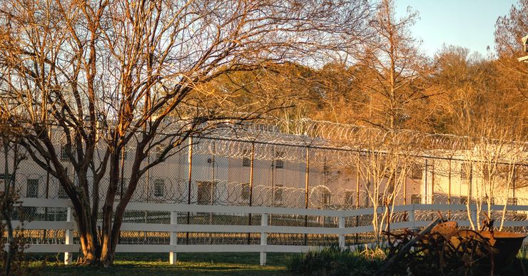 A barbed wire fence surrounds a tan-colored building. 