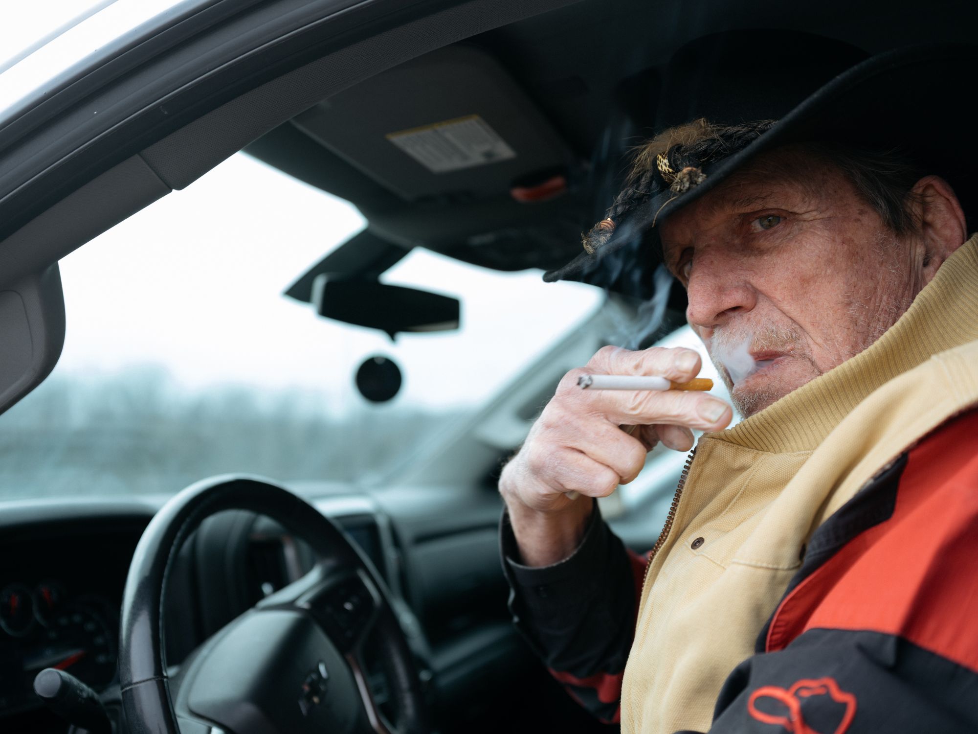 George Hall, a White man, smokes a cigarette while sitting in the driver's seat of a car.