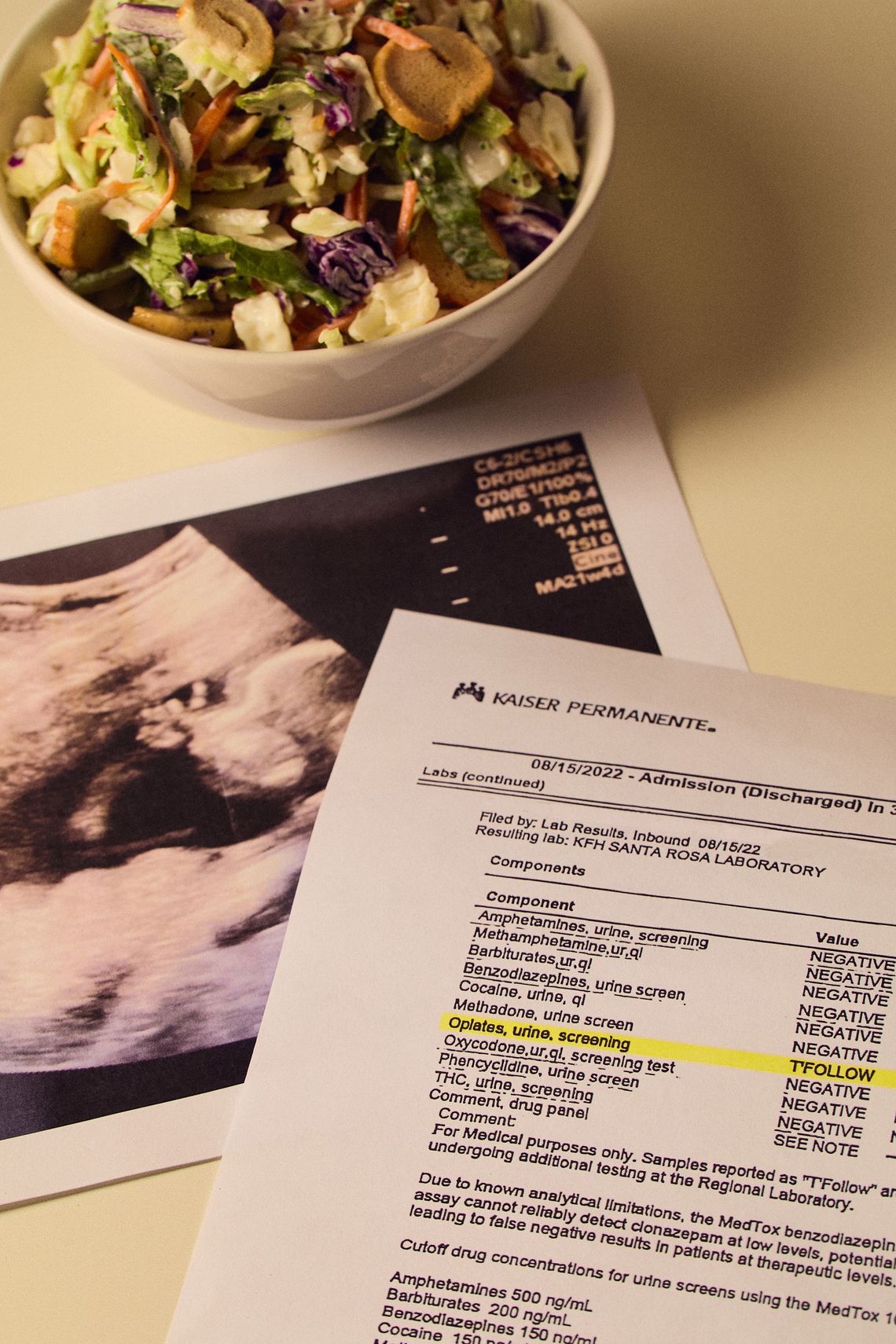 Three items are arranged on a white surface: a salad in a white bowl, a copy of a sonogram, and a printout of positive drug test results.