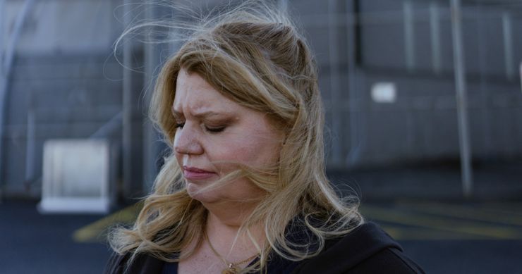 A photo shows a White woman, Sandra Hafraoui, with medium-length blonde hair, standing outside Delaney Hall, an ICE detention center. She is wearing a black, zip-up hoodie sweatshirt, and metal fencing and a two-story building is visible behind her.  