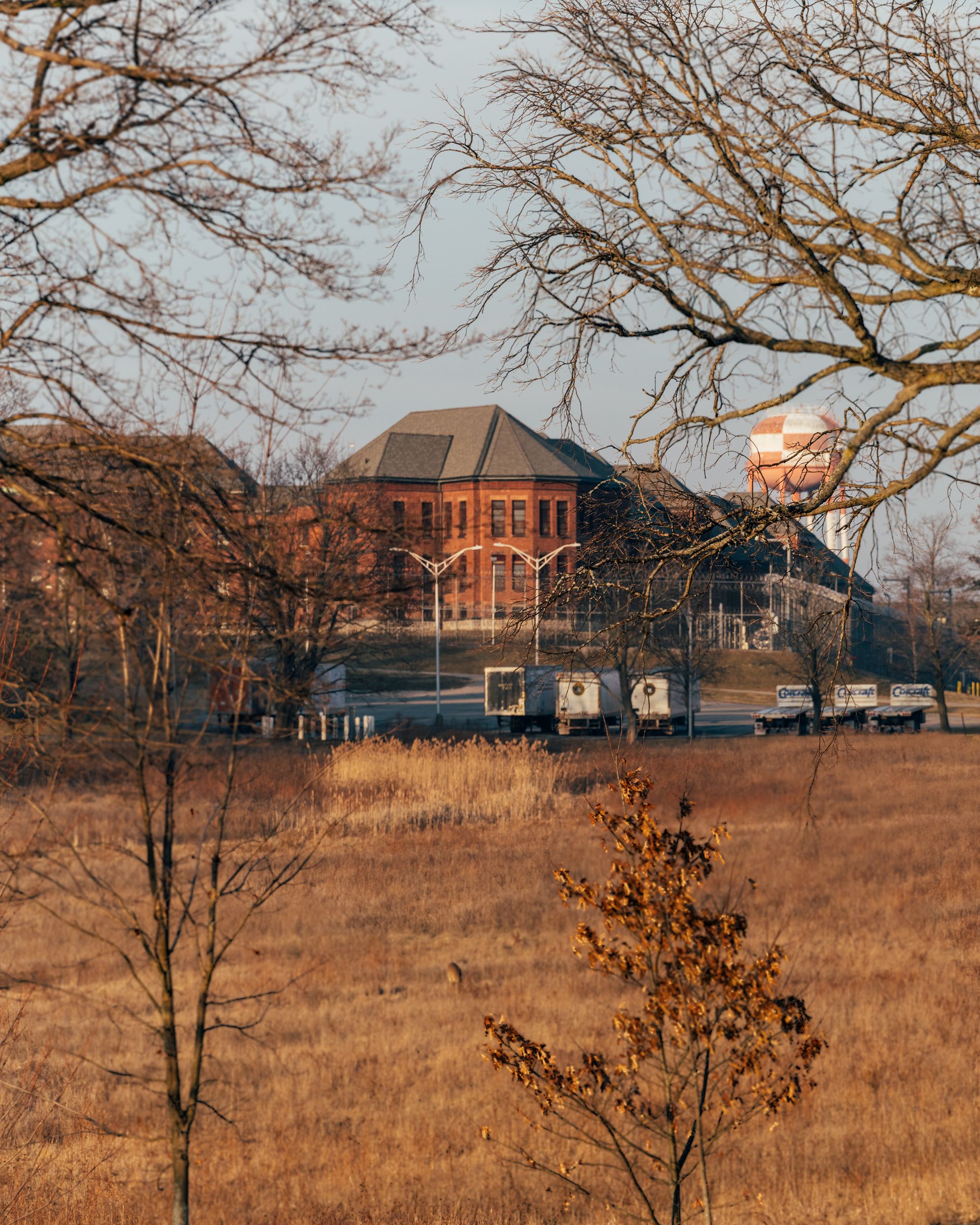 Fishkill Correctional Facility has brick walls and a gray roof behind a field of dried grass. 