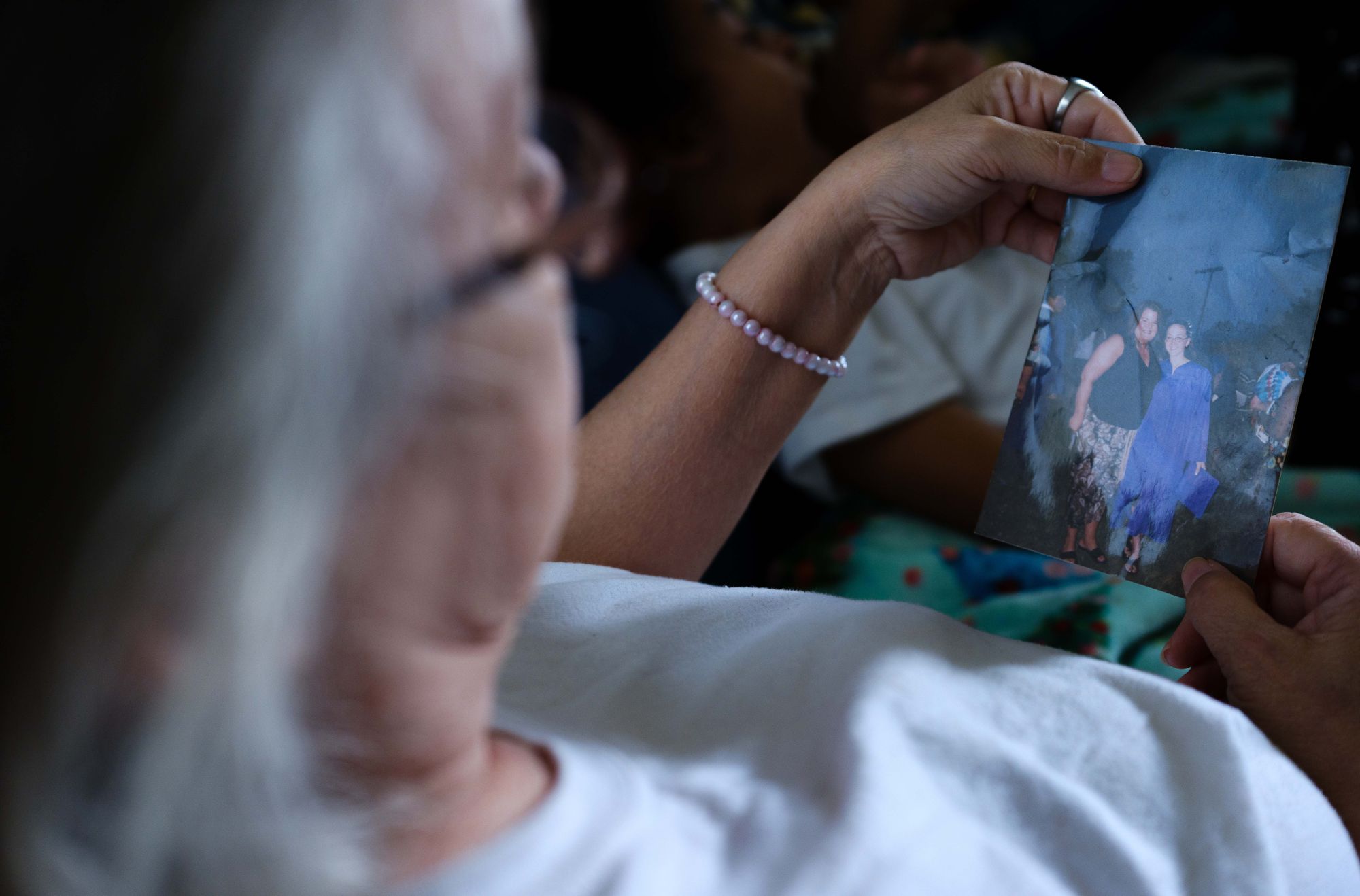 A White woman with light blonde hair looks at a photo she is holding in her hands of her daughter in a blue graduation gown.