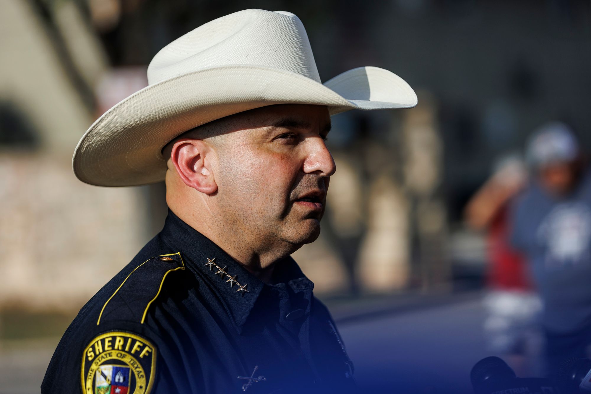 A photo of a man with medium-toned skin, wearing a cowboy hat and a navy blue sheriff's uniform.  