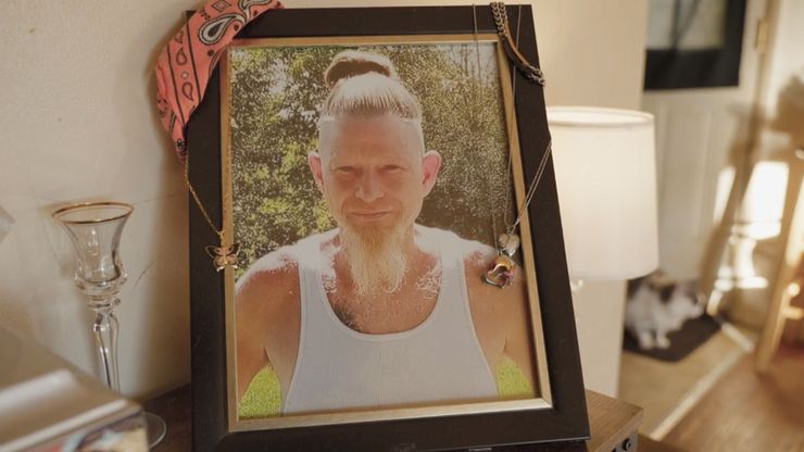 A portrait of a White man smiling and wearing a tank top is mounted inside of a picture frame.