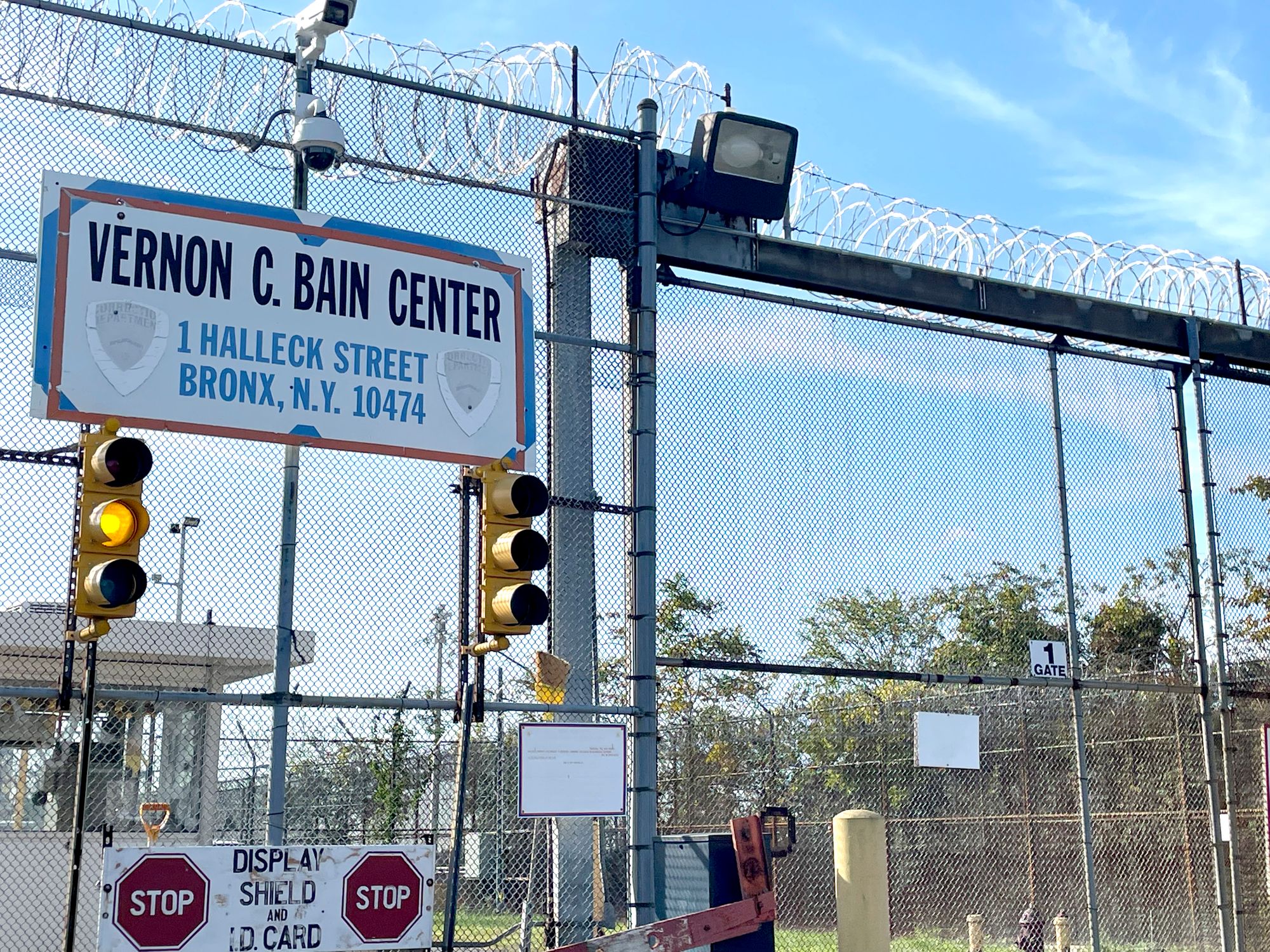 The entrance to a New York correctional facility, with the sign “Vernon C. Bain Center” on a tall wired fence with barbed wires.