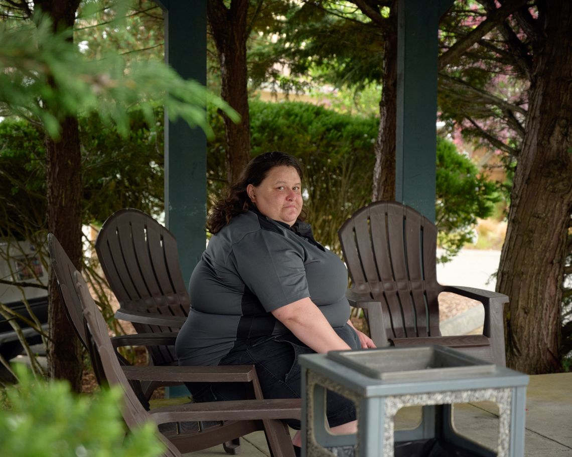 A woman with light-toned skin and medium-length, brown wavy hair sits in a chair at the Port Ludlow Resort, where she works. 