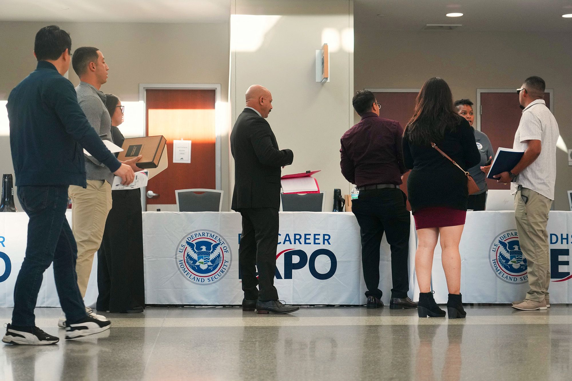 Several people dressed in business attire line up in front of a booth at a hiring event. 