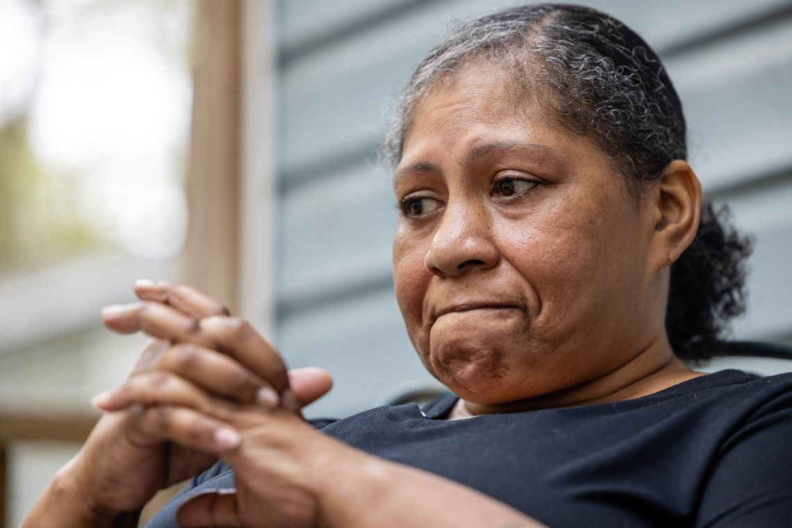 A photo of a frowning Black woman looking off camera with her hands clasped. 