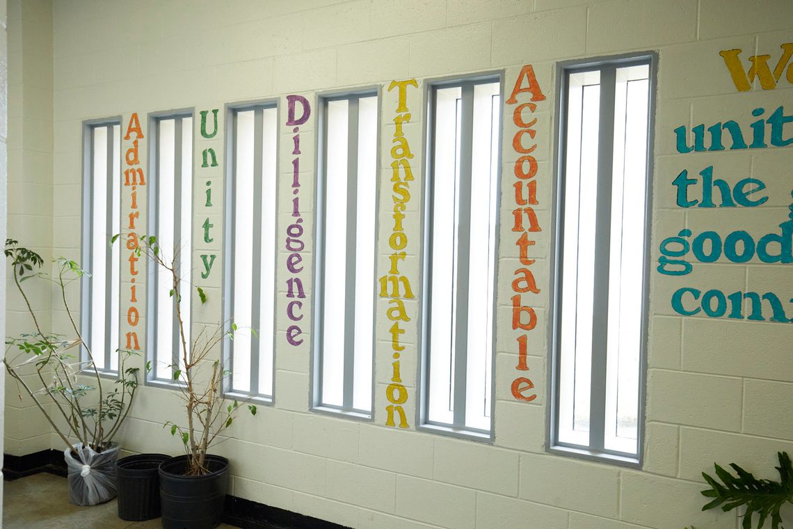 A room with six narrow, vertical windows shows words painted between each window reading: “Admiration”, “Unity”, “Diligence”, “Transformation” and “Accountable” in different colors.