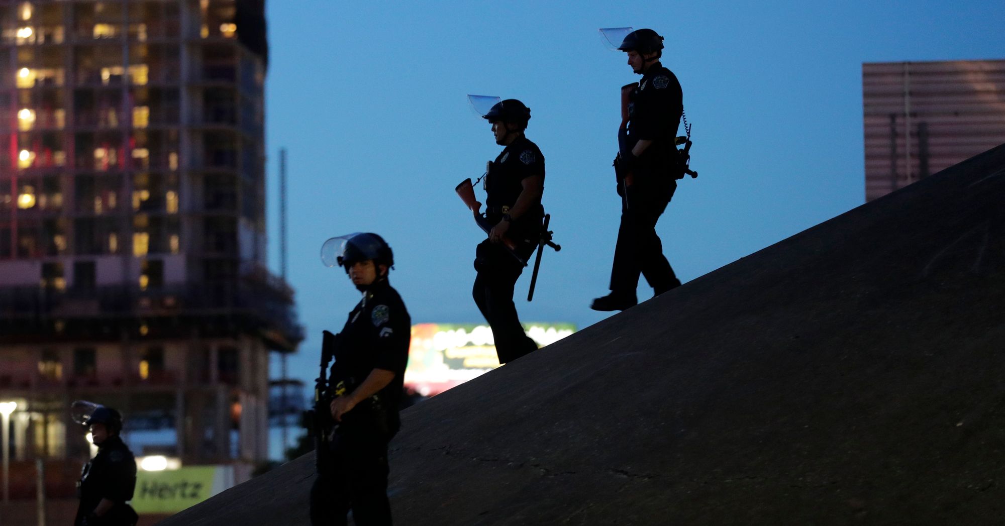 Three police officers in riot gear walk down a slope outdoors.  