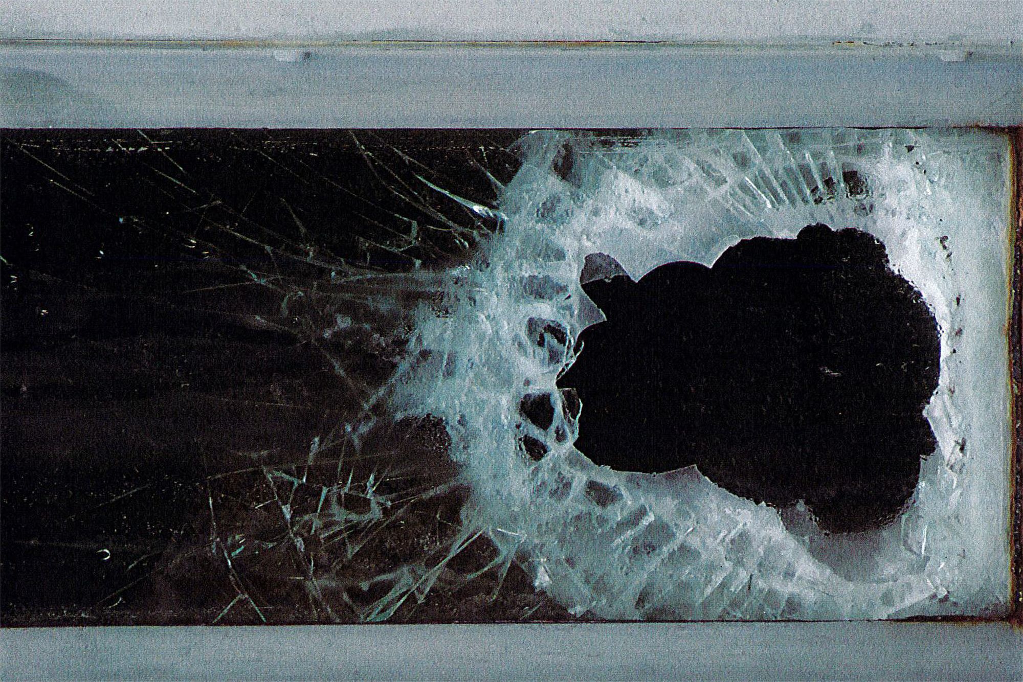 A photo shows a hole in a window, surrounded by cracked glass. 