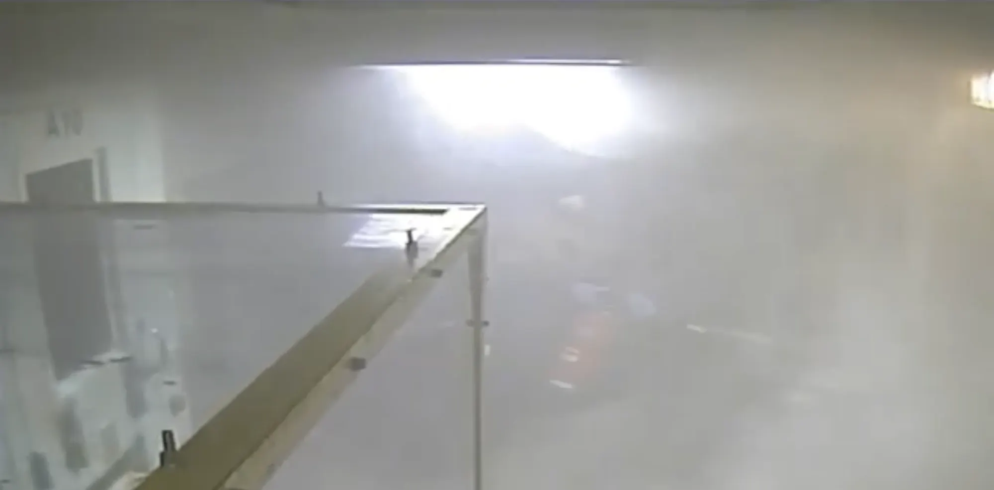 A video still shows a hallway filled with thick smoke. Barely visible, a correctional officer sprays a fire extinguisher at a prison cell door.