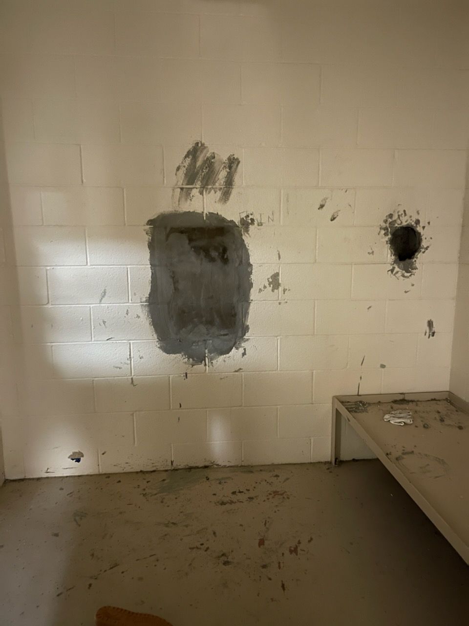 The wall of a cell shows an area with gray exposed paint in the shape of a hole. 