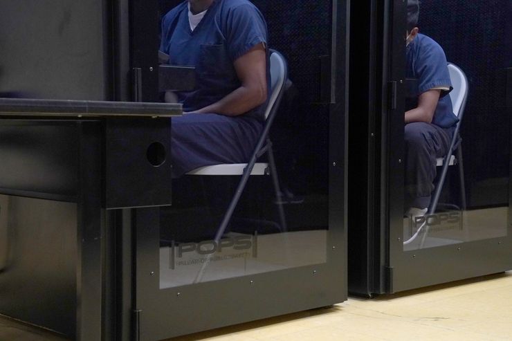 Two detainees in blue uniforms, whose faces are not showing in the photograph, sit in privacy booths talking to their attorneys or asylum officers. 