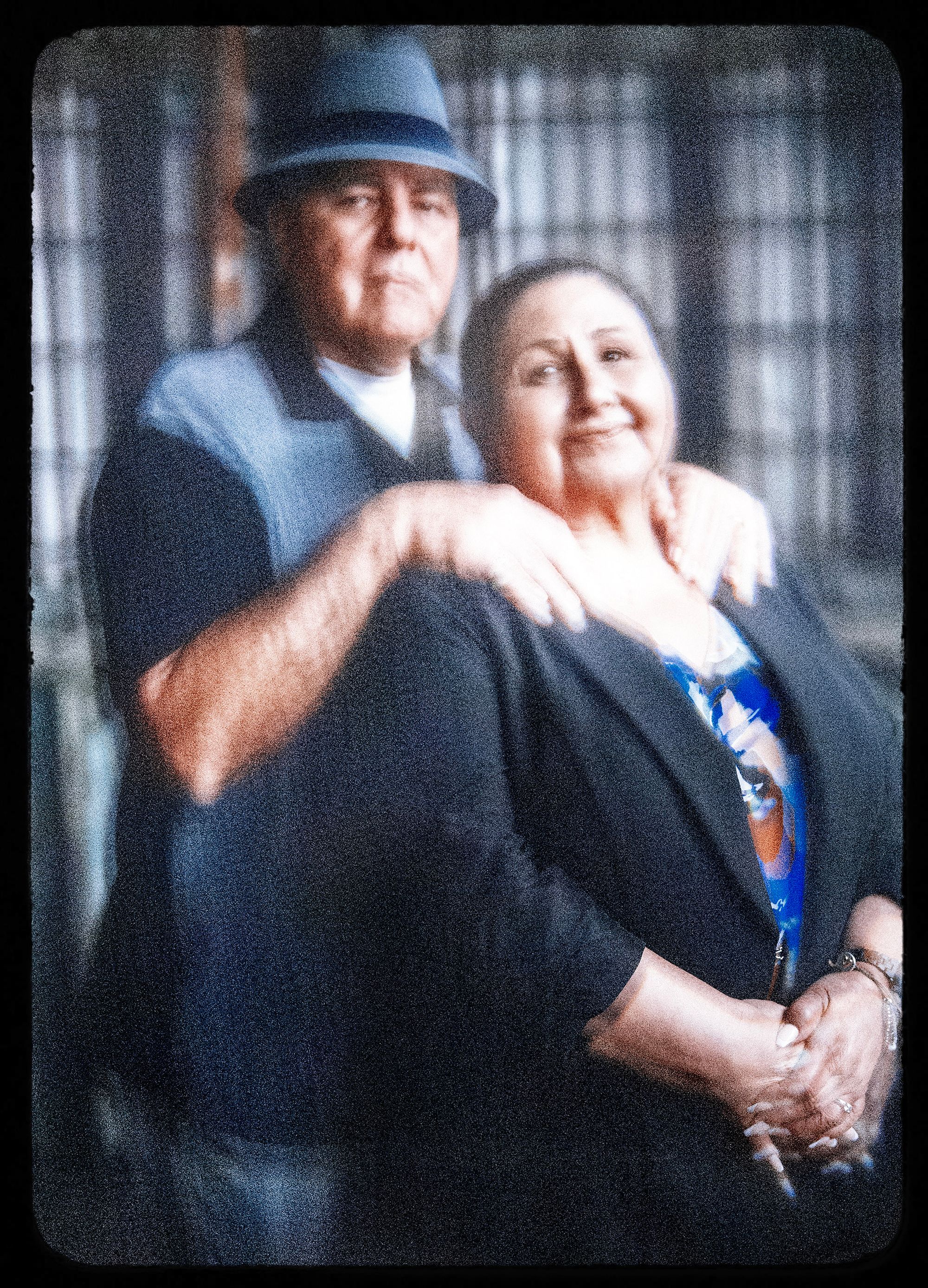 A photo shows Jack Morris and Dolores Canales, standing in a warehouse. Morris, a man wearing a grey hat and a black-and-grey short-sleeved shirt, stands behind Canales, a woman wearing a black blazer and a blue patterned shirt. The photo has a shaky effect achieved using a lens.