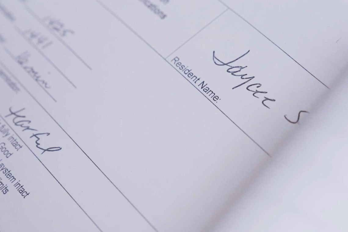 A photo shows a close-up of a paper record with “Jaycee S” handwritten in the field for “Resident Name,” and the word “tearful” handwritten on a line below. Part of the record is out of focus. 