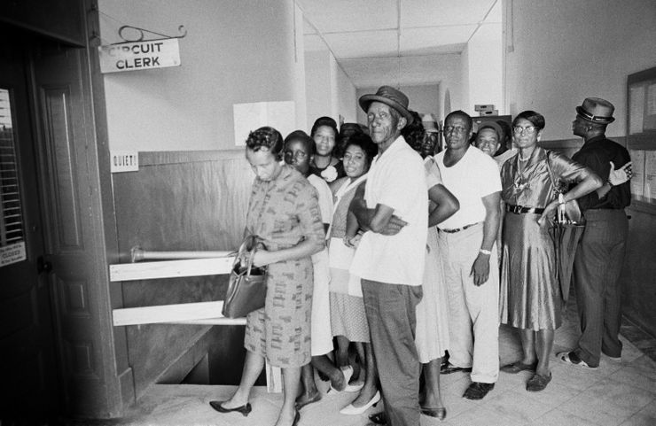 A black-and-white photo shows a group of Black men and women waiting in line under a sign that says “circuit clerk”.