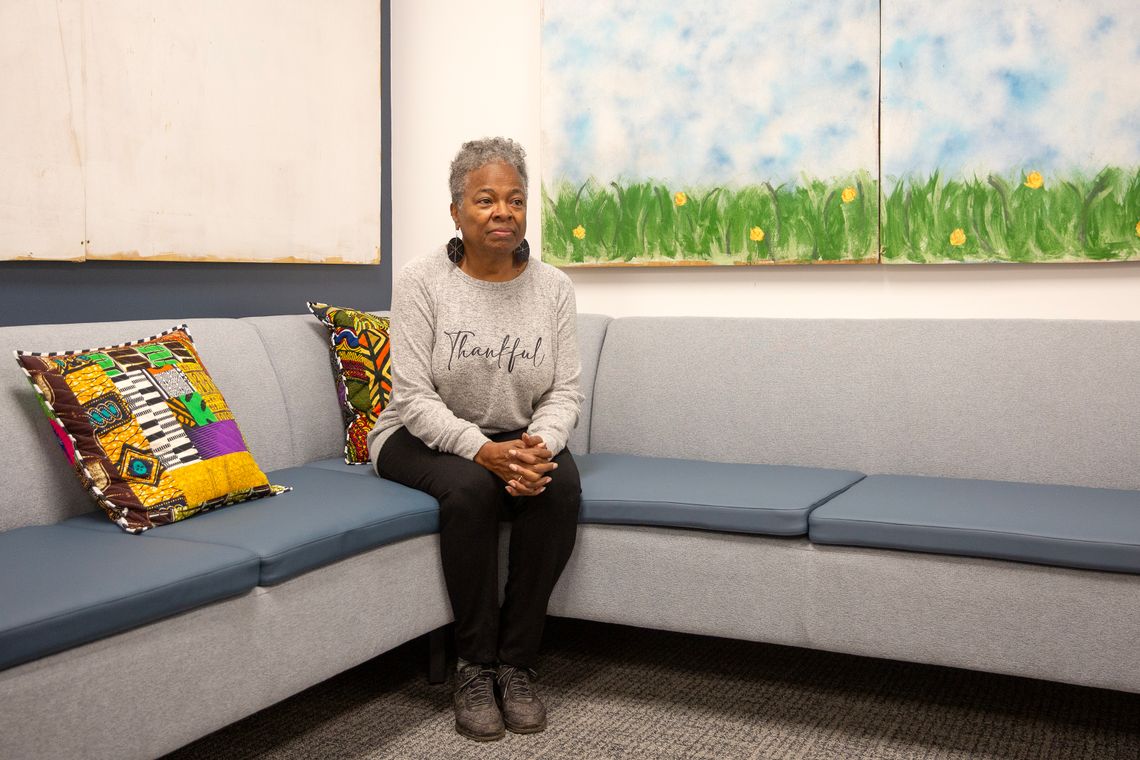 A Black woman with gray hair wearing a heathered gray sweater that reads “Thankful” looks away from the camera.