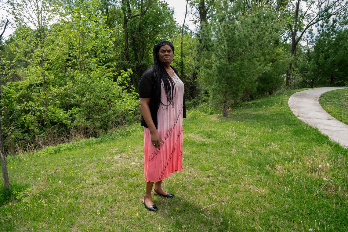 A Black woman with braids and a pink dress stands on a lawn.