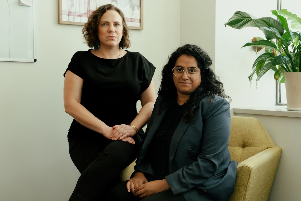 Two attorneys, a White woman and an Indian woman, pose for a portrait in their office.