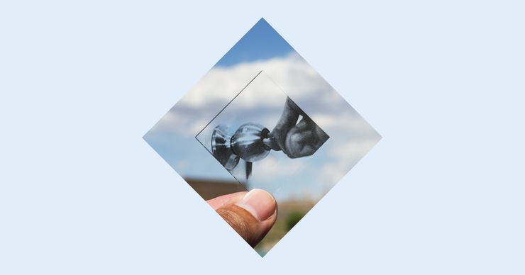 A diamond with a transparent slide held up by a hand against the sky depicting a hand opening a doorknob with a key.