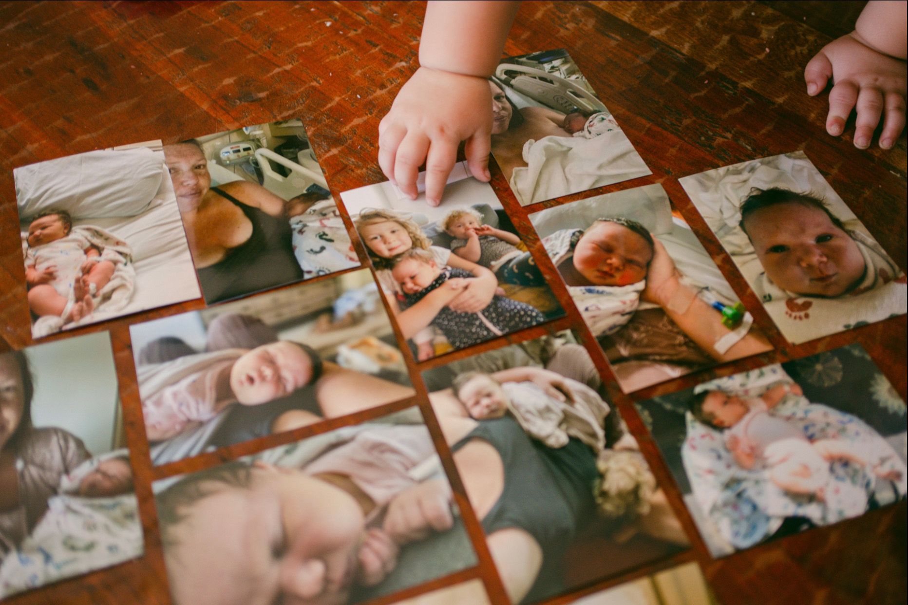 Twelve photos are arranged on a wooden floor showing Susan Horton, a White woman, with her newborn and two of her other children. A toddler's hand is touching one of the photos.