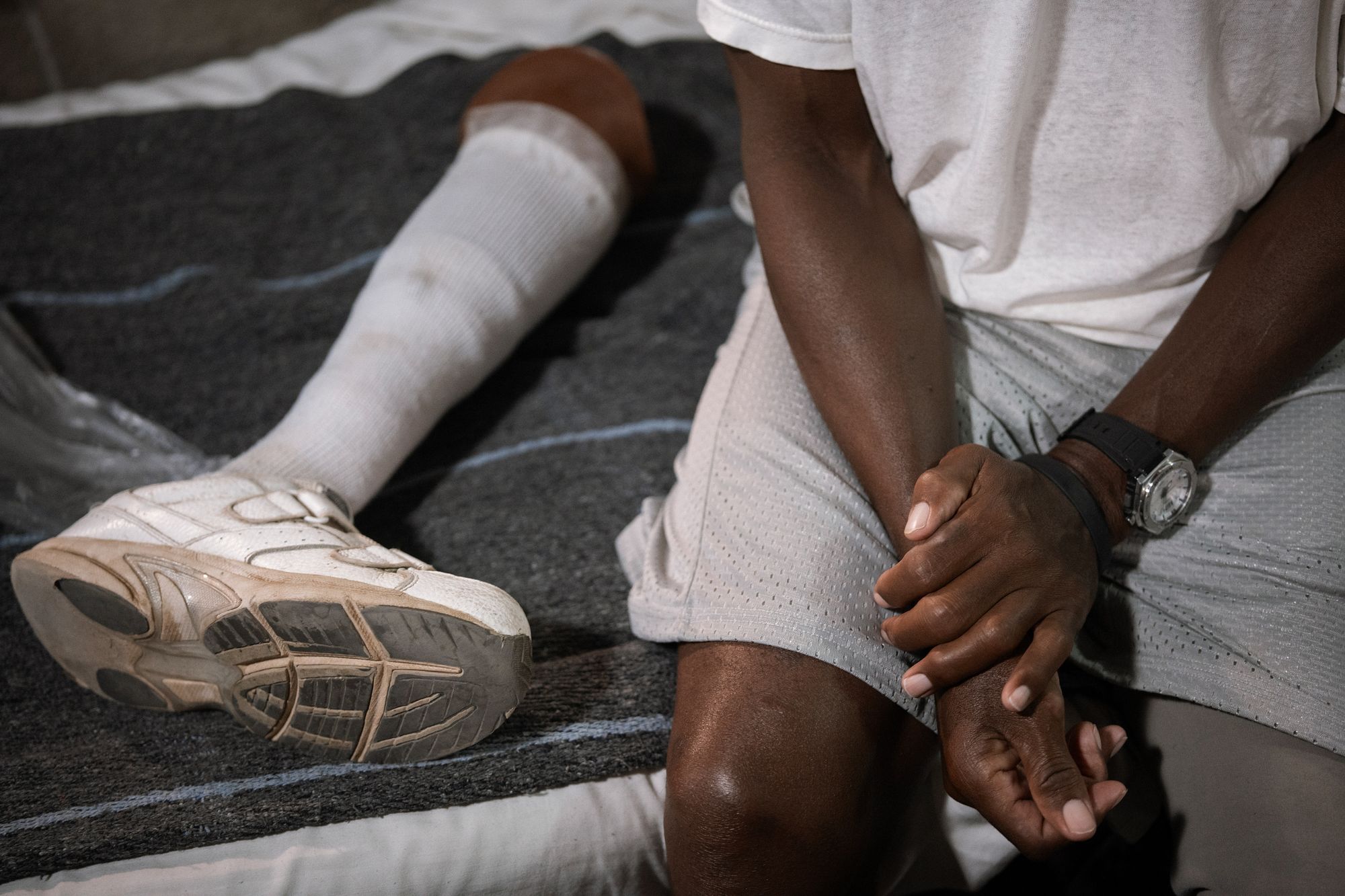 A photo shows a Black man sitting on his bed, while a prosthetic leg lies next to him. 