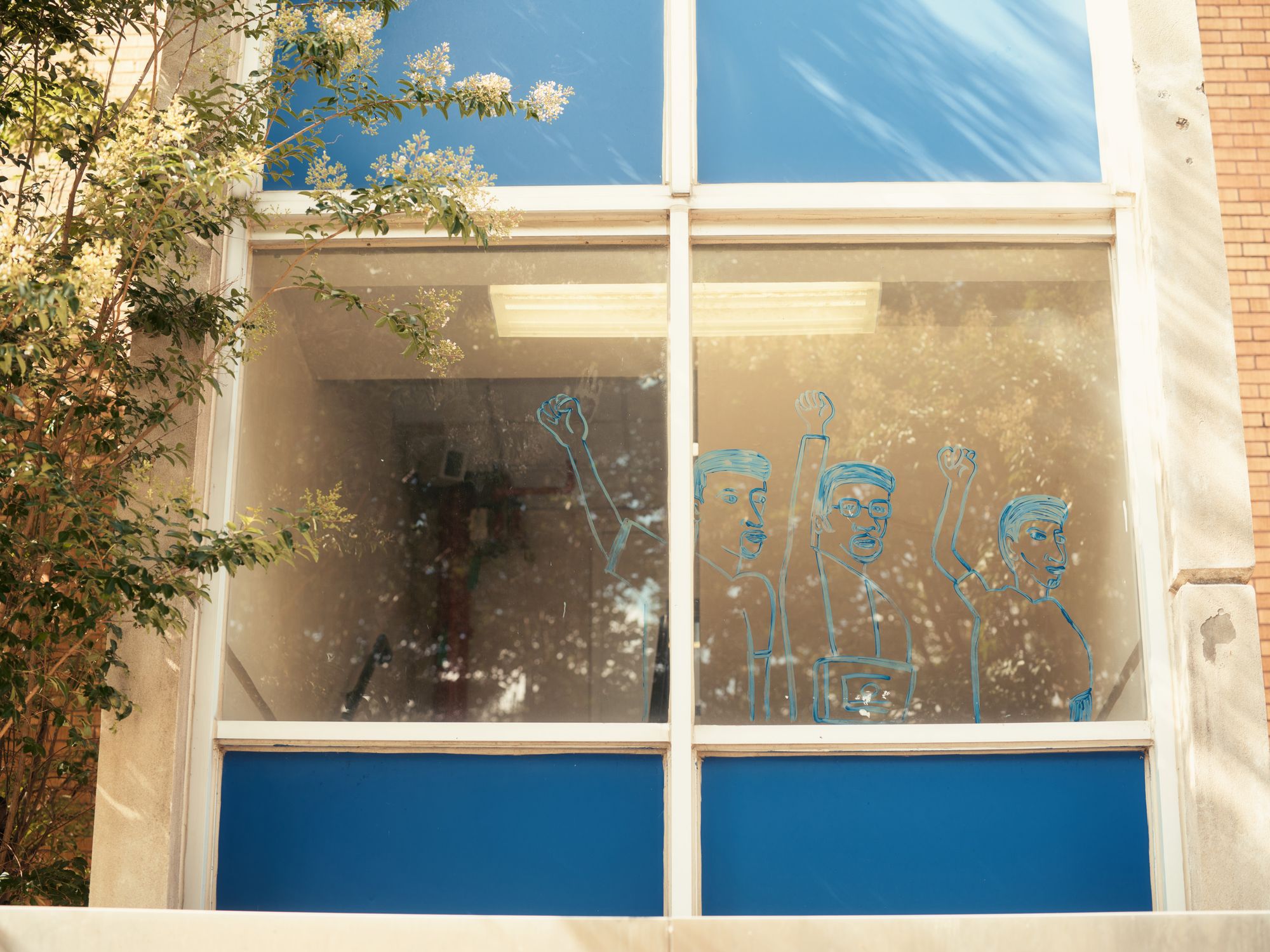 A photo shows the outline of three people with their fists raised, drawn in blue paint on a window. 