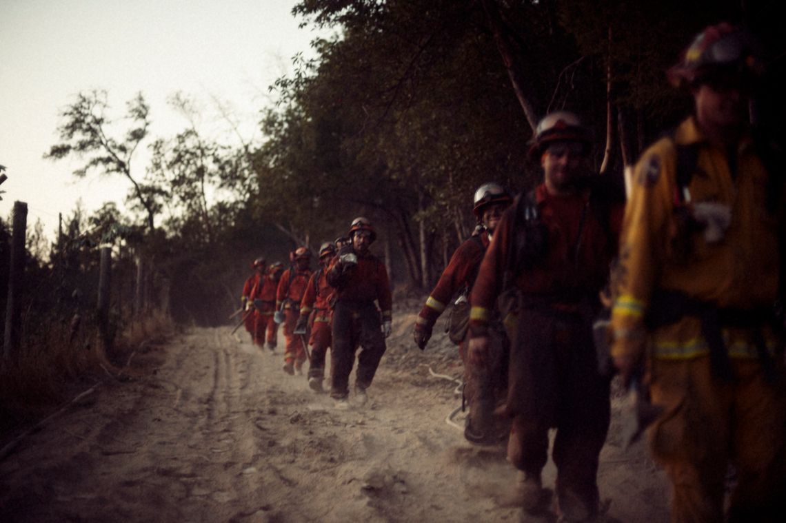 Several firefighters are walking on a dirt path in a line.