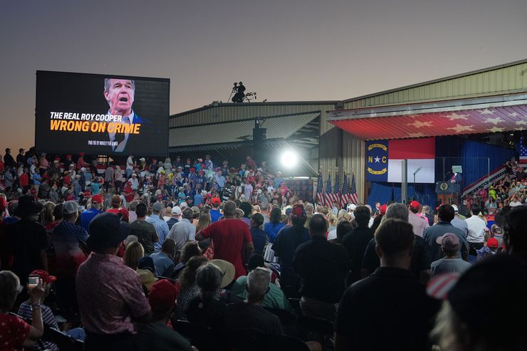 A photo shows hundreds of people standing at a campaign rally as they look at President Donald Trump standing at a podium. 