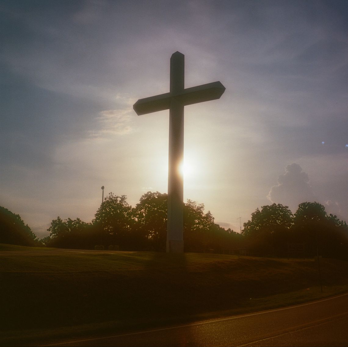 A triptych of three color photos of a large cross next to a road and a church. 
