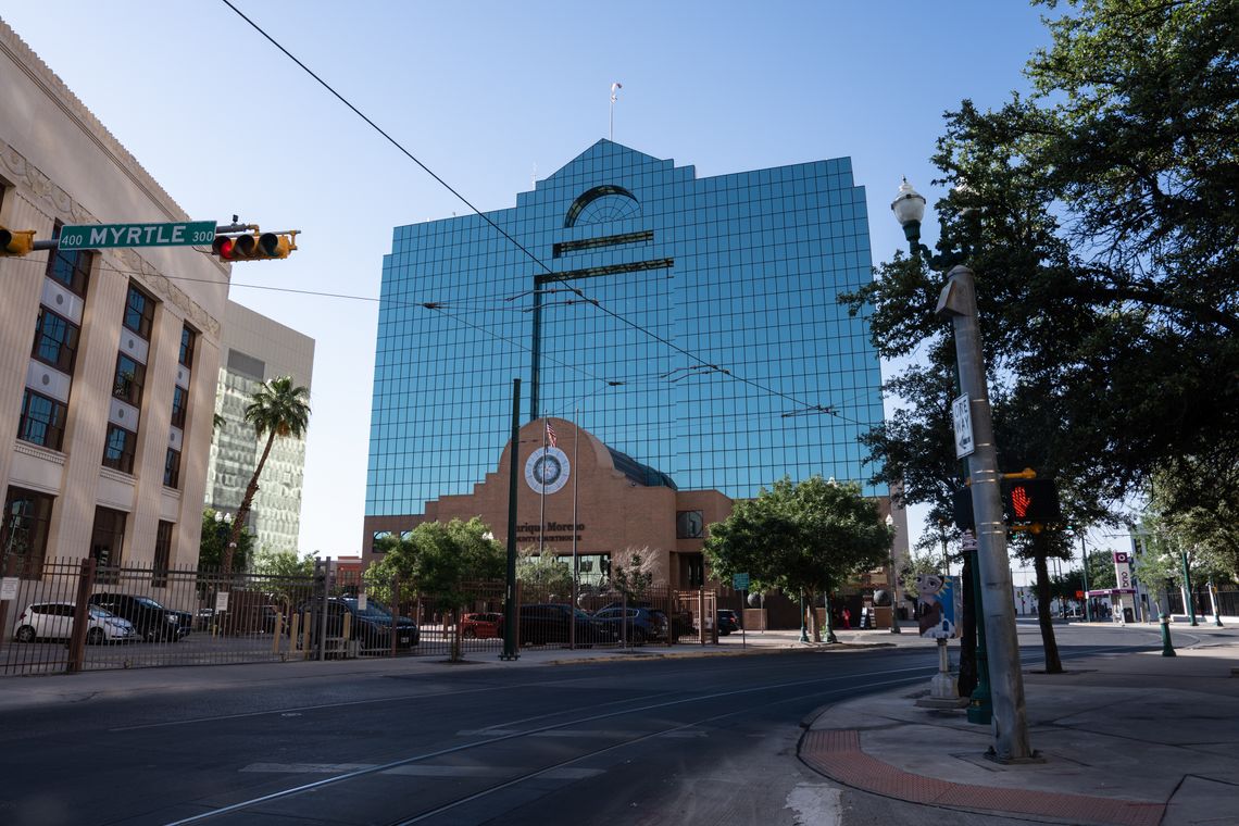 A photo shows the El Paso County Courthouse, a low brick building, in front of a tall building with a glass facade. A traffic light is in the foreground, as well as a street sign that says “Myrtle.” 