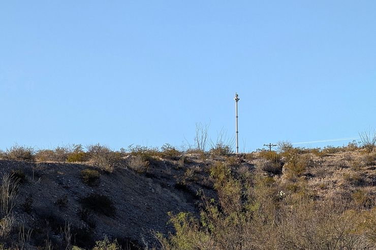 A photo shows a white surveillance tower at the top of a hill. 