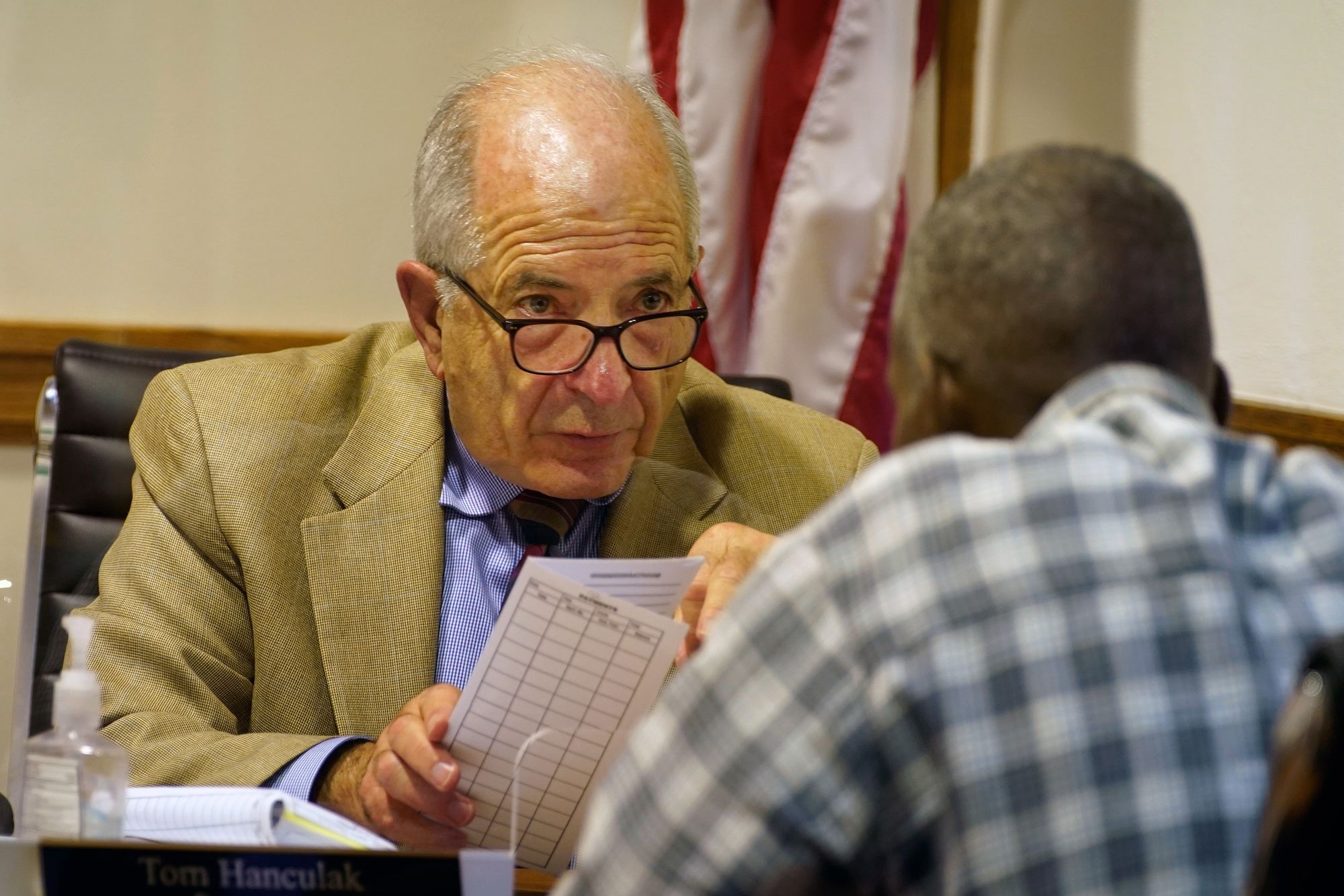 Prosecutor Tom Hanculak, a White man with short white hair and glasses, talks to a Black man in a plaid shirt. 