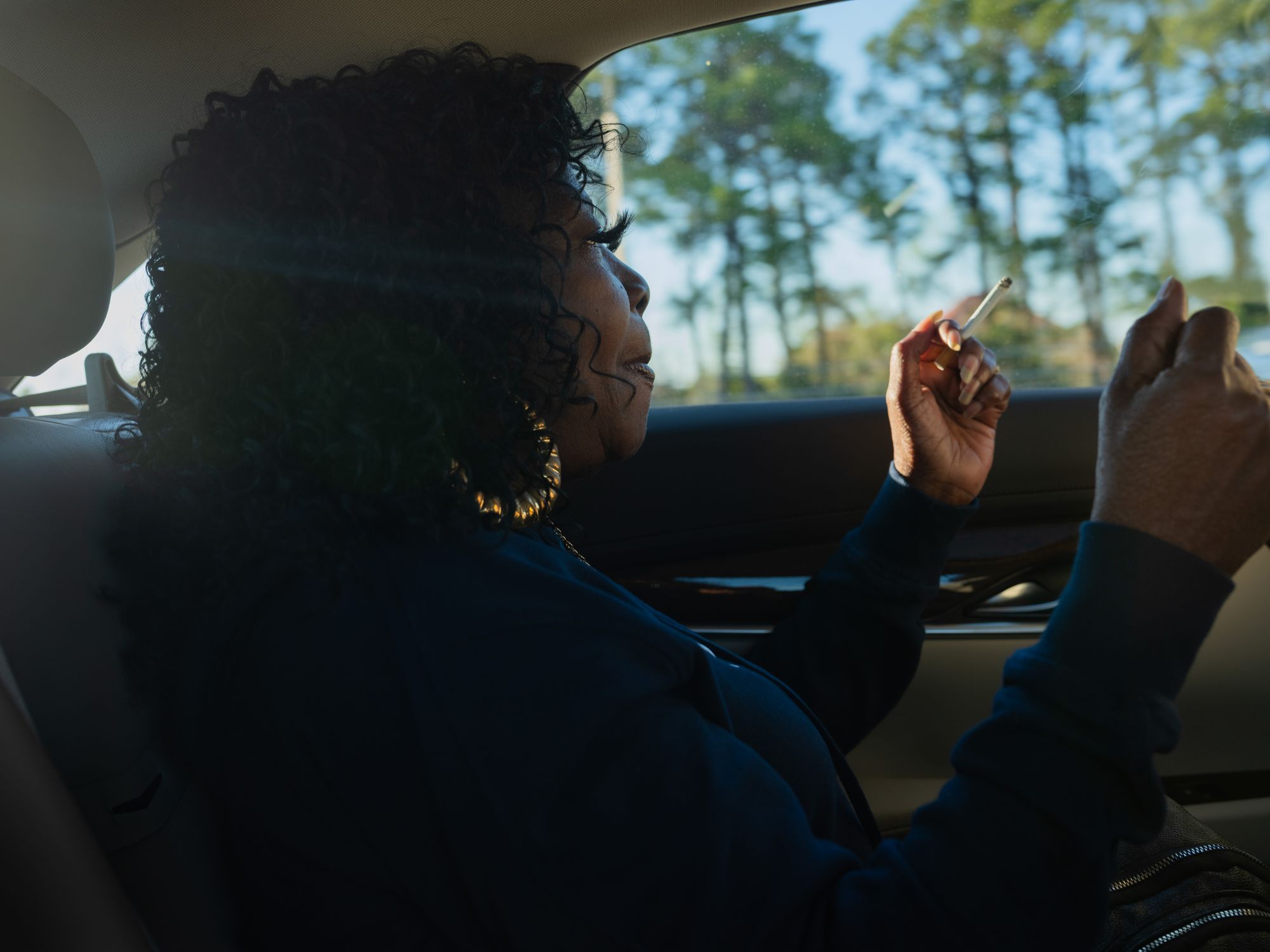 Armour sits in the backseat of a car, looking out a window while holding a cigarette.