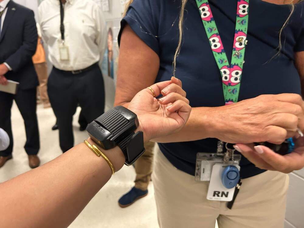 A photo shows a black electronic device attached to the wrist of a person with medium skin tone. 
