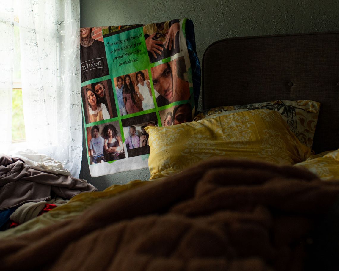 A photo of a green blanket with family photos and text hanging up near a bed with yellow pillows. 