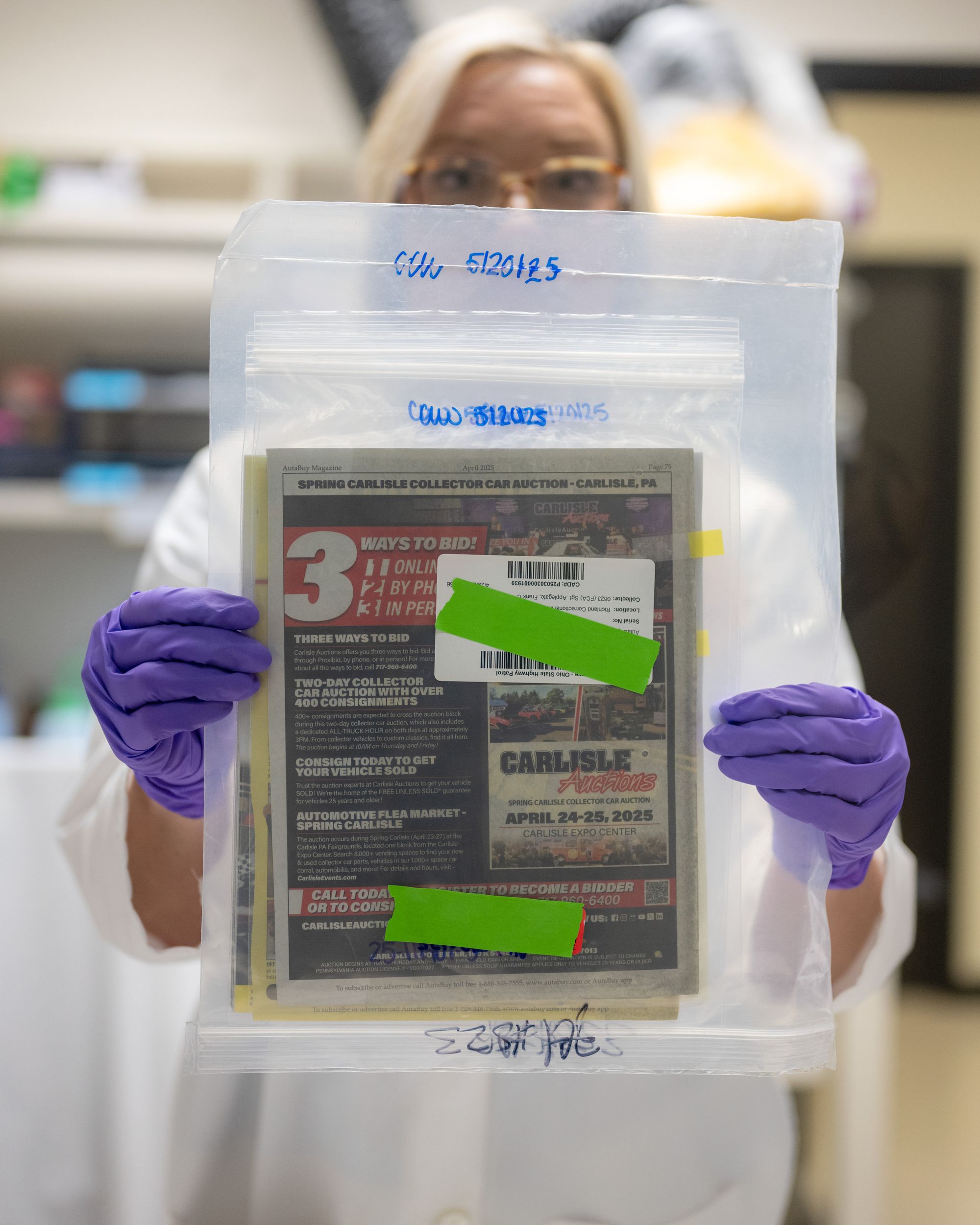 A photo shows a White woman with blonde hair wearing a lab coat and purple gloves holding up a plastic bag that has some papers and folders in it. 