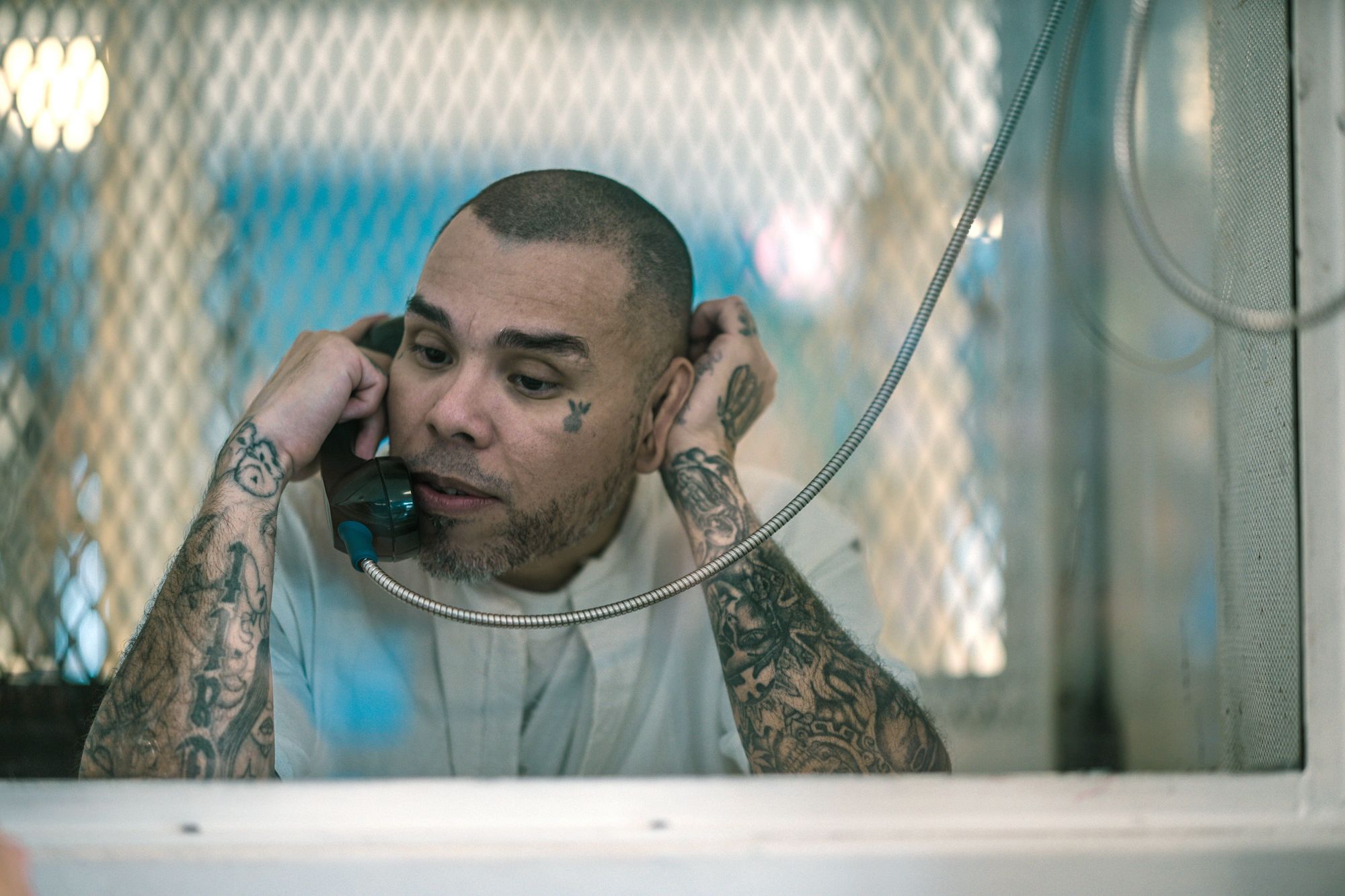 A light-skinned Hispanic man with close-cropped hair and tattoos on his arms uses the phone at the Polunsky Unit prison facility.