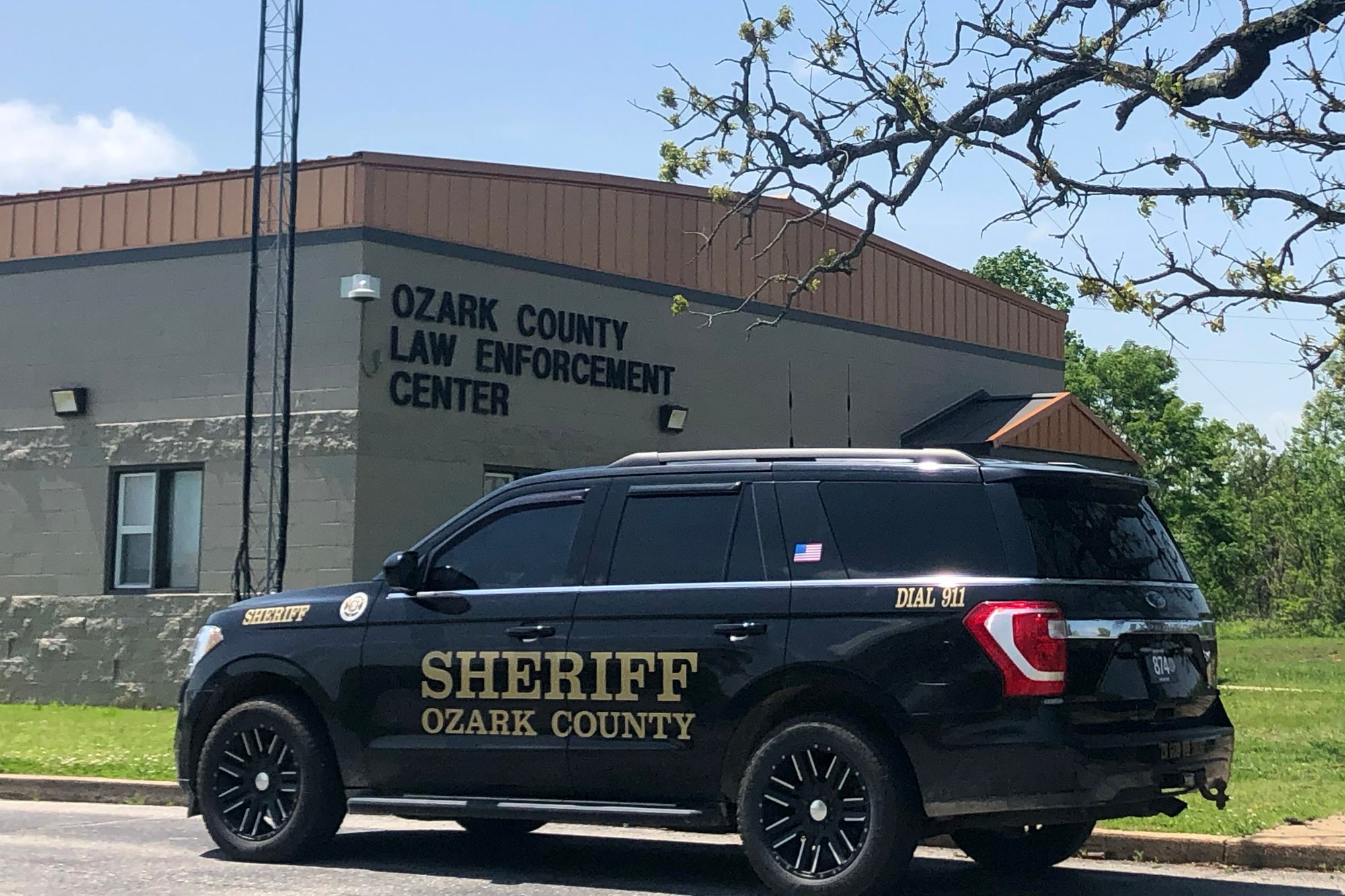 A Black SUV with the words “Sheriff Ozark County” on the driver’s door is parked in front of a gray brick building with a sign that reads “Ozark County Law Enforcement Center.” 
