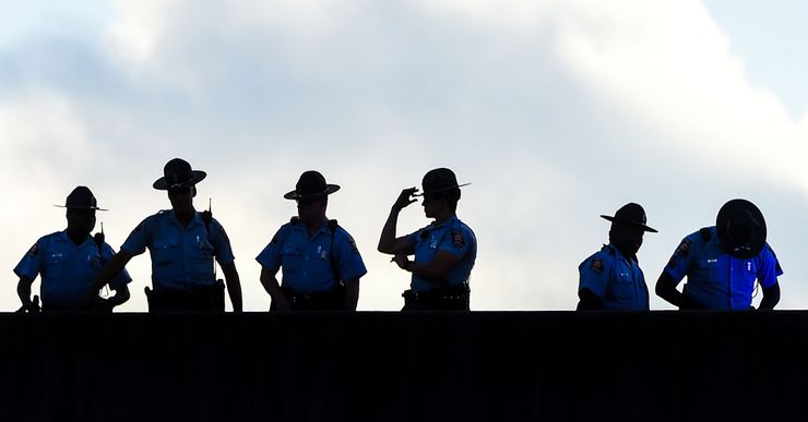 An image shows the silhouettes of six police officers standing on a bridge against a cloudy background.