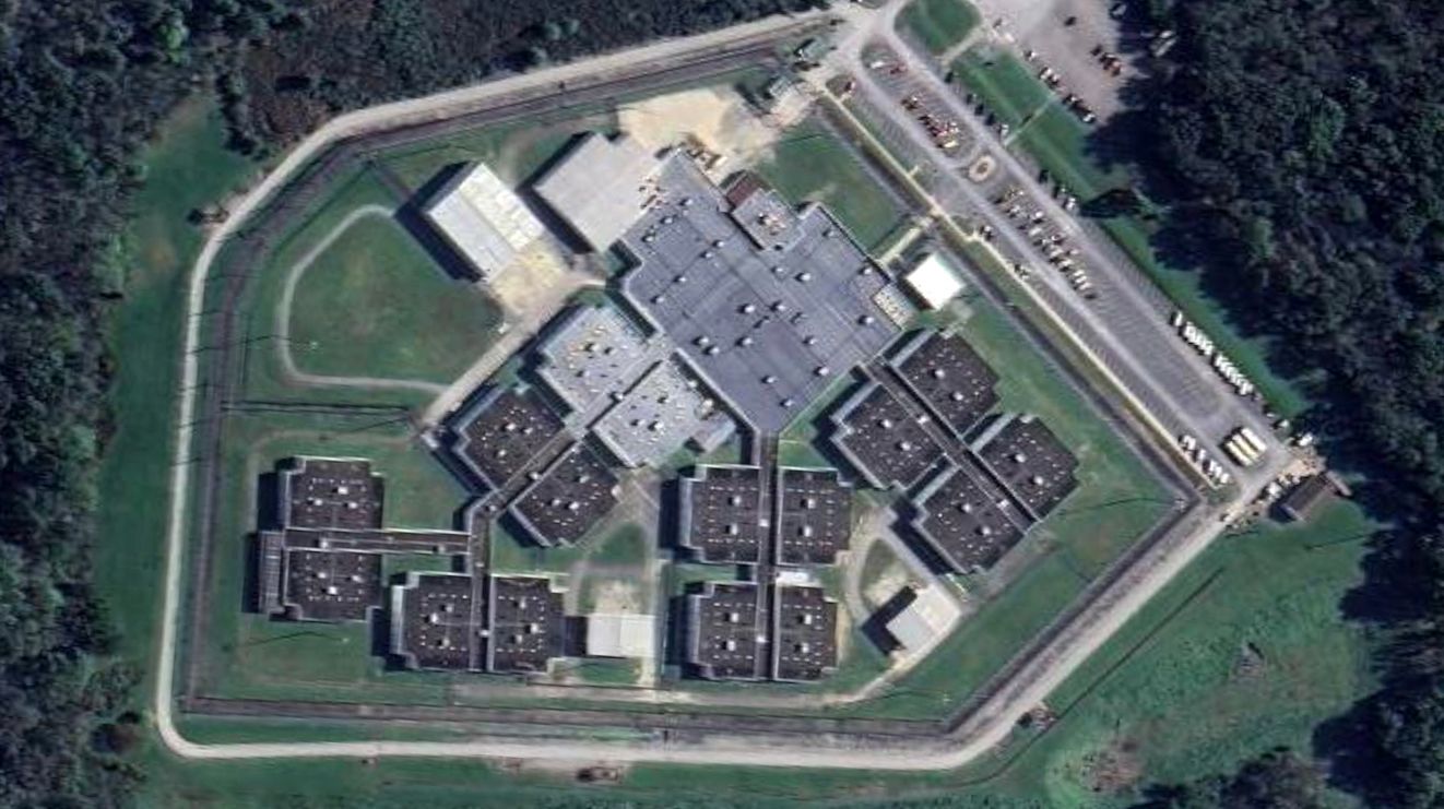 A photo shows an aerial view of the Northeast Ohio Correctional Center, which is composed of more than a dozen buildings. The complex is surrounded by trees. 