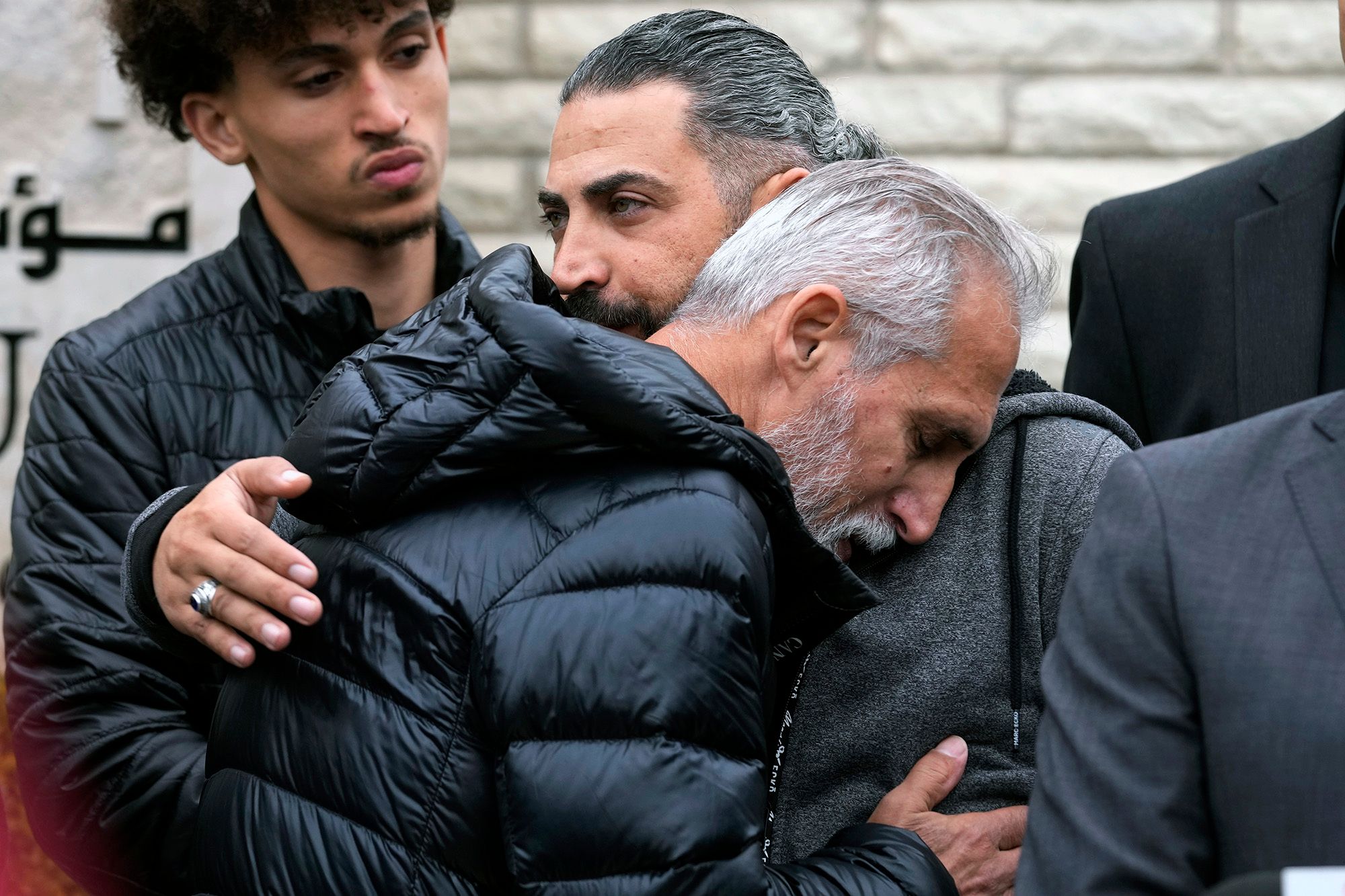 A Palestinian man pats the back of an elderly Palestinian man as he hugs him. 