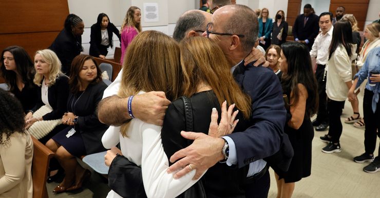 A group of two men and two women hug in a courtroom full of people.  